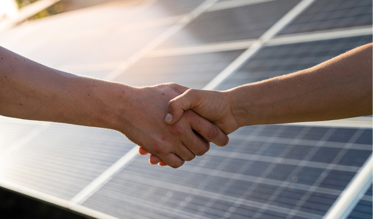 Business agreement symbolized by a handshake, with a solar panel in the background representing renewable energy collaboration.