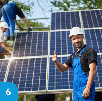 Solar panel installers at work, one staff member giving a thumbs up to the camera as a sign of successful installation.