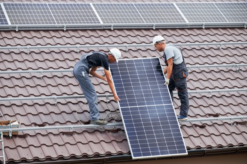 Men technicians lifting up photovoltaic solar moduls on roof of house. Engineers in helmets building solar panel system outdoors. Concept of alternative and renewable energy.