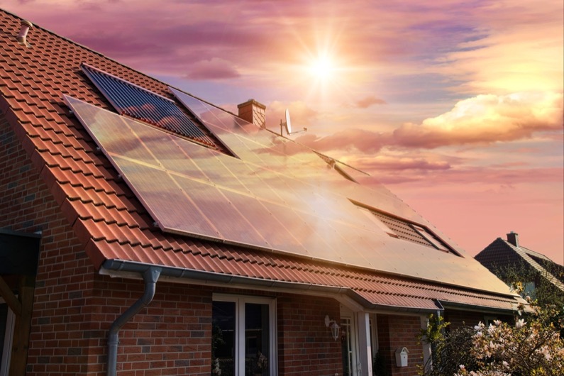 Photo collage of solar panels, photovoltaics on the red roof of a house and a beautiful sky with the setting sun. 