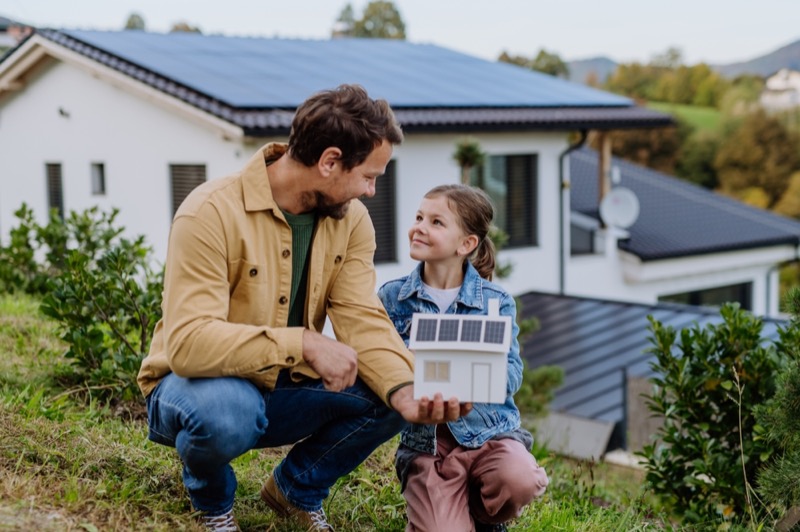 Little girl with her dad holding paper model of house with solar panels, explaining how it works.Alternative energy, saving resources and sustainable lifestyle concept.