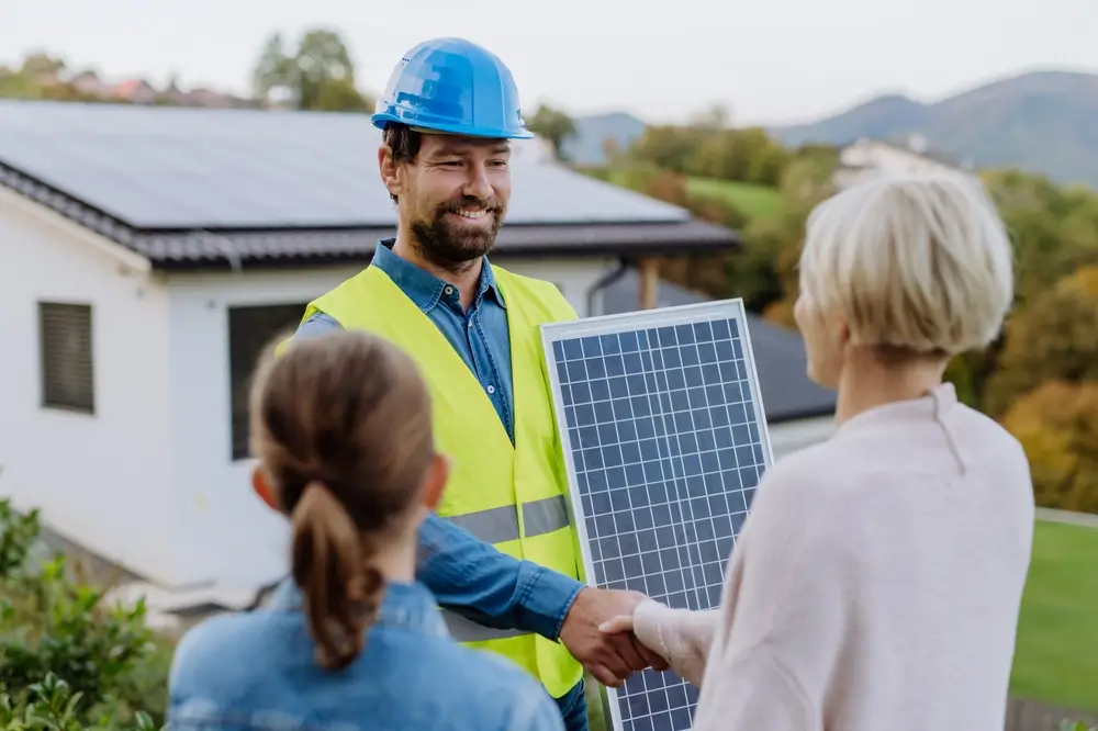 Smiling handyman, photovoltaics panels installer shaking hand with family owner of house.