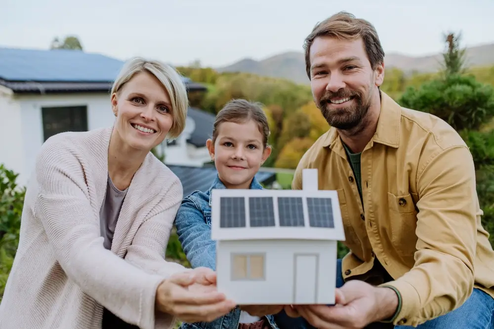 Happy family holding paper model of house with solar panels.